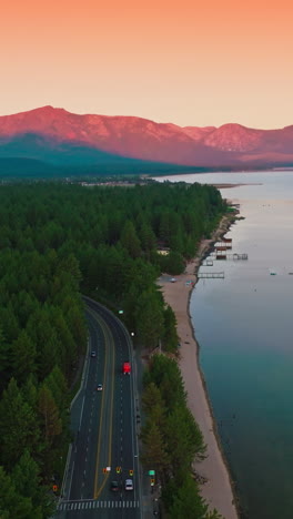wooded shore of the lake tahoe with wide road through the forest. pink mountains and pink skies at backdrop. top view. vertical video