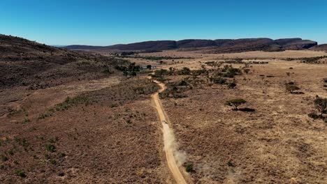 Off-road-adventure-through-rugged-terrain-in-a-remote,-scenic-wilderness-under-a-blue-sky,-drone-view