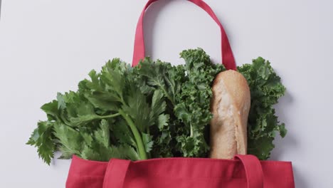 video of red canvas bag with parsley, kale and baguette, copy space on white background