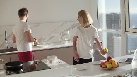 Beautiful-young-caucasian-man-preparing-breakfast-for-two-in-kitchen-at-home-and-mixing-eggs-in-bowl,-wife-coming-over-and-kiss