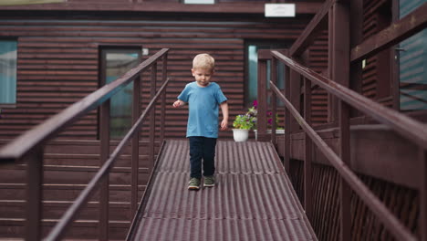 little boy goes down wooden ramp holding on railing at hotel