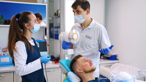 teacher holding dental device talks to his student. male patient lies in the chair. dentistry practice.