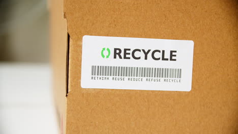 hands applying recycle sticker label on a cardboard box with barcode rethink reuse reduce refuse