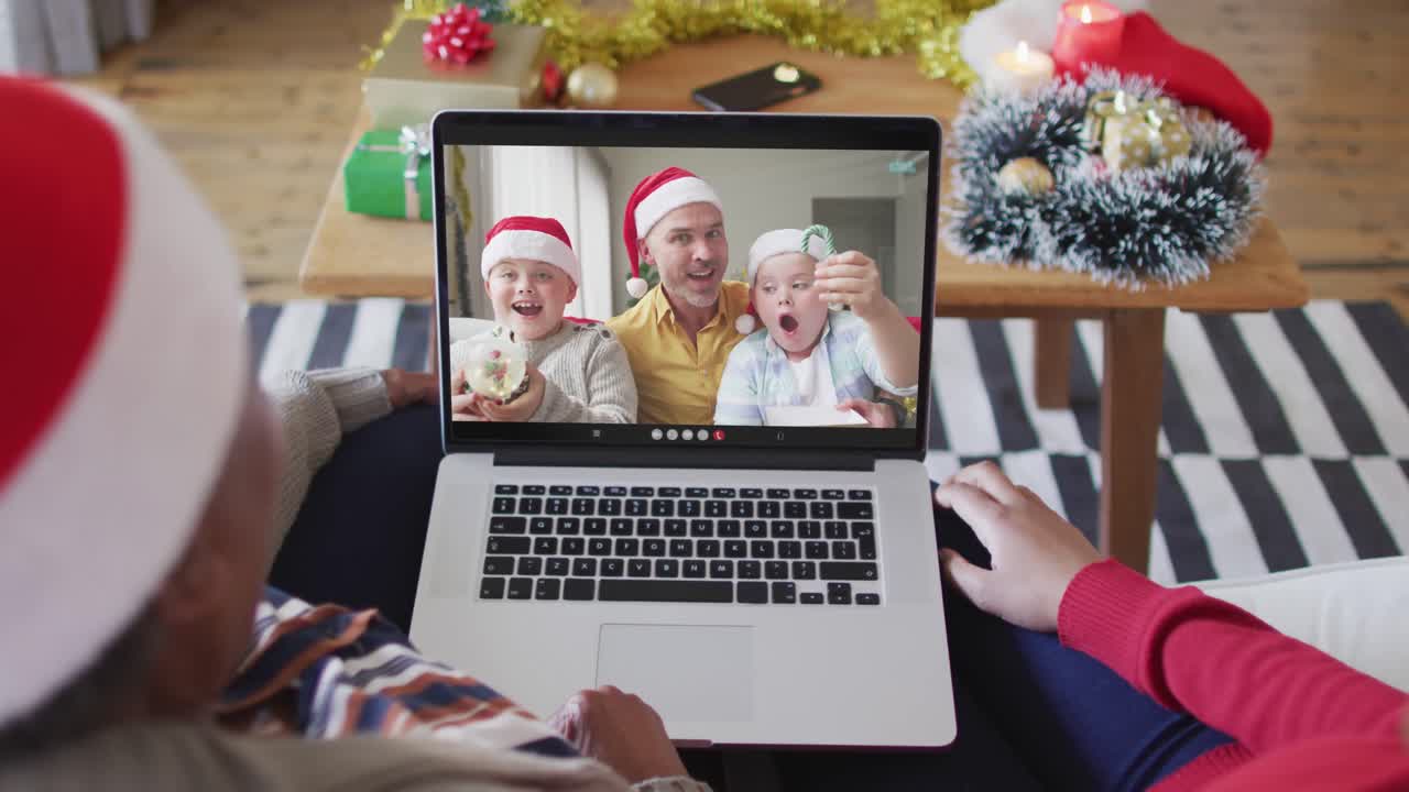 madre y hija afroamericanas usando una computadora portátil para una videollamada de navidad con la familia en la pantalla