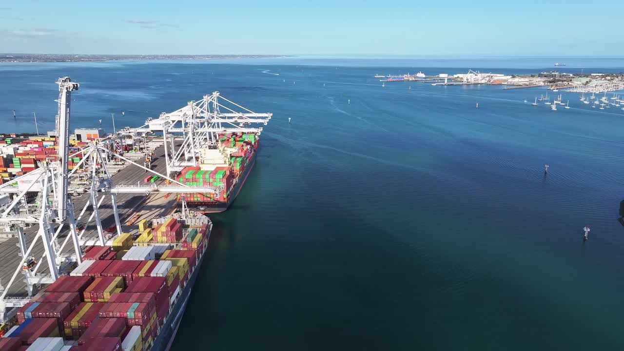 Cargo vessel docked beside cranes at Melbourne container port with clear coastal waters