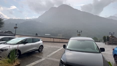 wide shot of rain and hail hitting a car during the day in the street of gavarnie gedre village in the wild pyrenees mountain national parc