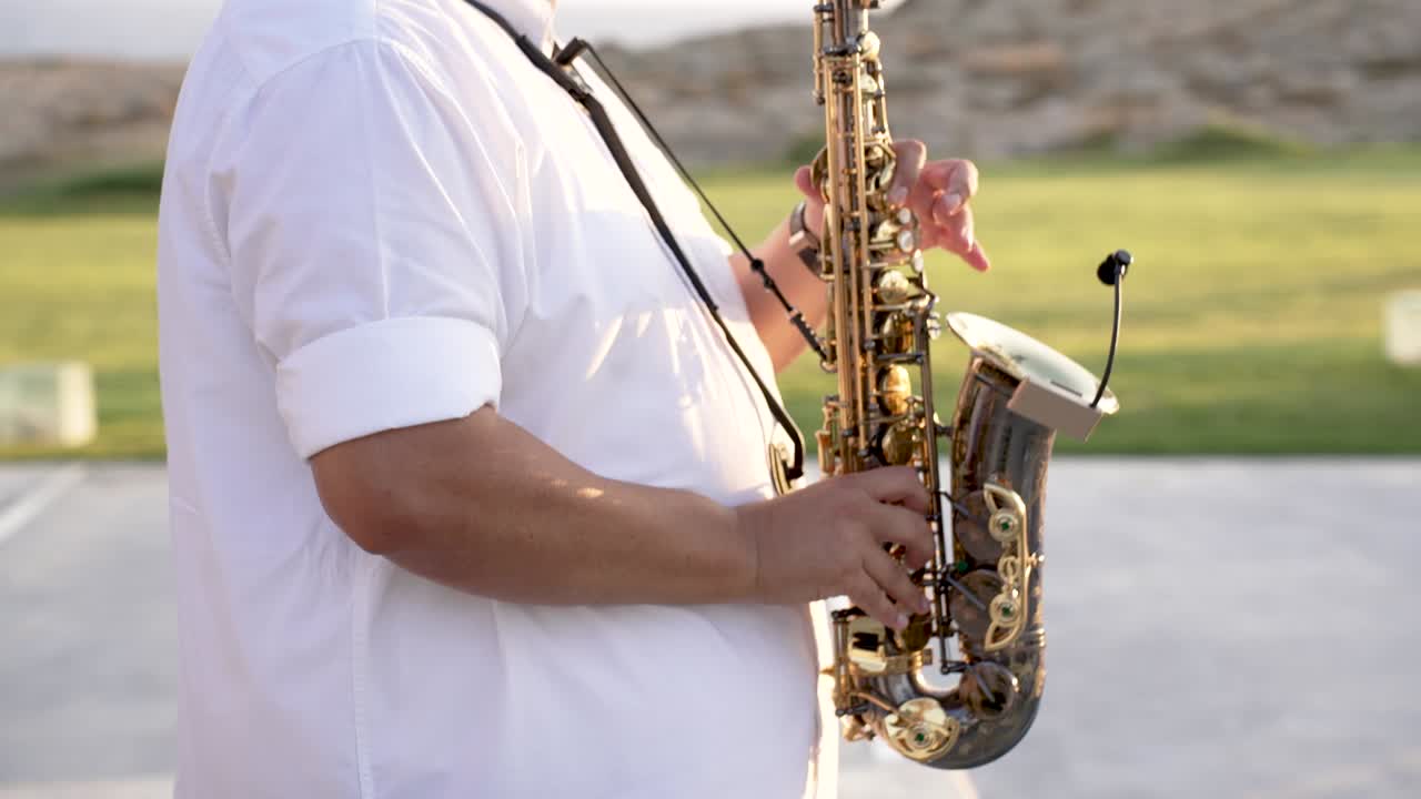 Un musicista suona il sassofono in un parco pubblico mentre il sole tramonta sullo sfondo. L'area è aperta, con vegetazione e cielo sereno visibili