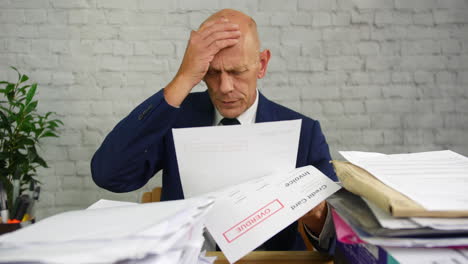 a stressed man with headache opening a stack of bills and letters with final notice for credit card debts