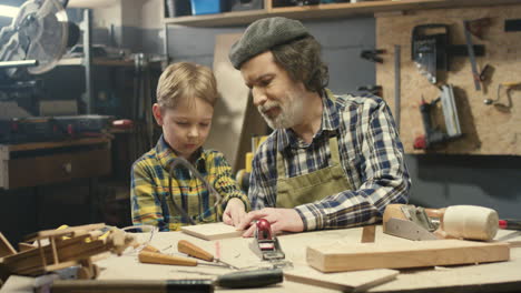 caucasian carpenter man teaching his little son to work with hardwood and sawing timber in workshop