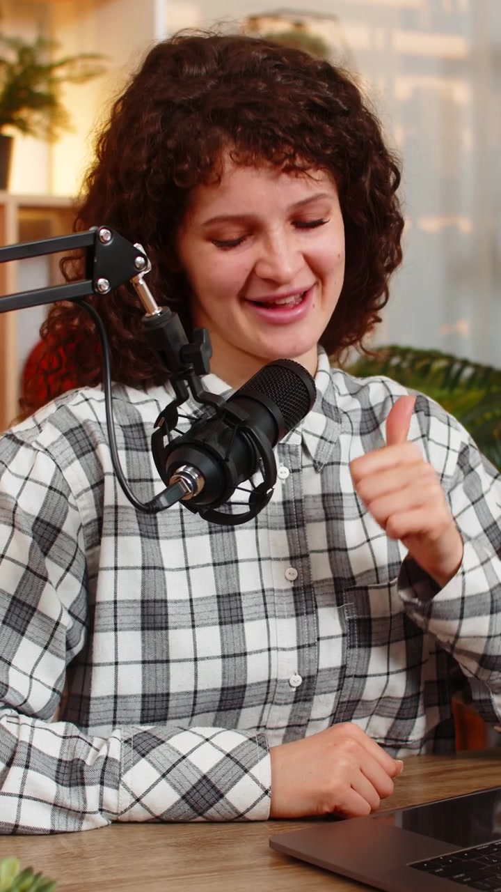 Young woman on home table recording live stream with laptop microphone and expressive hand gestures