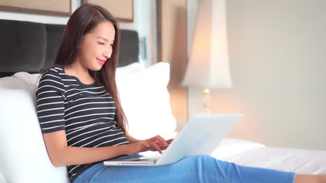 young asian woman working online on laptop computer from bedroom during lockdown