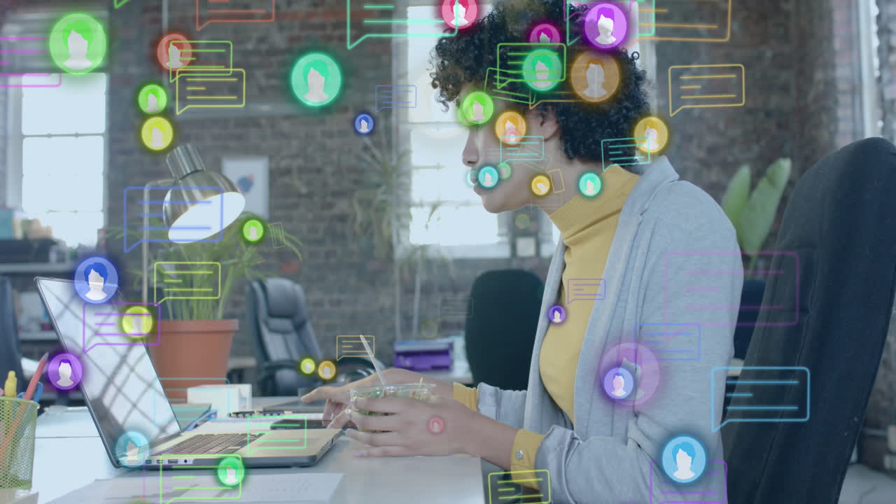 animación de iconos de los medios sobre una mujer de negocios biracial usando una computadora portátil y almorzando en la oficina