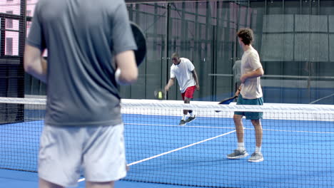Young diverse men playing padel tennis on blue on indoor court, focusing on intense match