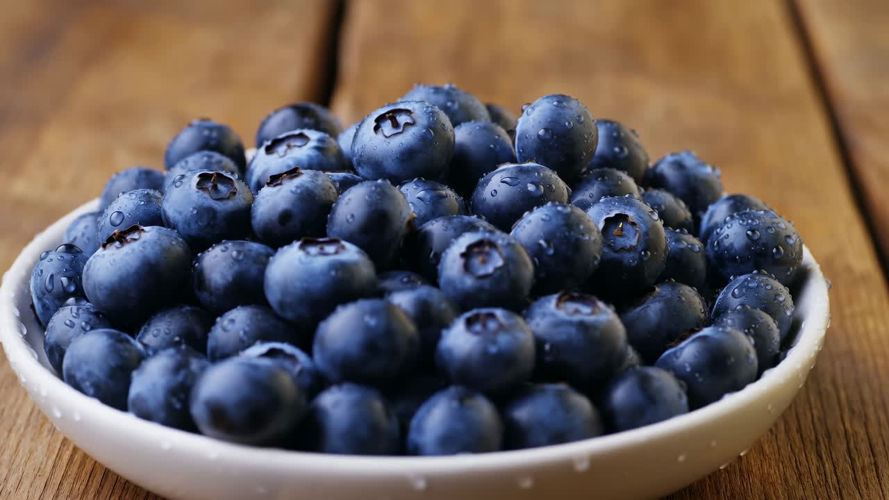 Close-up de tigela de mirtilos em mesa de madeira, frutas maduras orvalhadas empilhadas em prato branco, ambiente de café da manhã rústico com tons quentes.