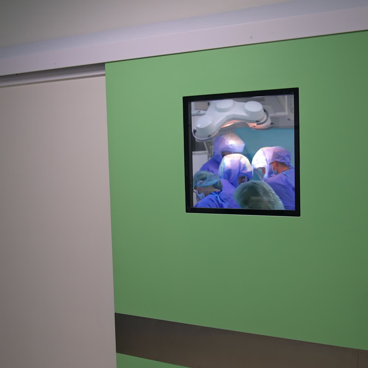 Sliding door with a window to the modern surgical room. Operation is taking place inside the ward. Nurse comes up to the door to close it