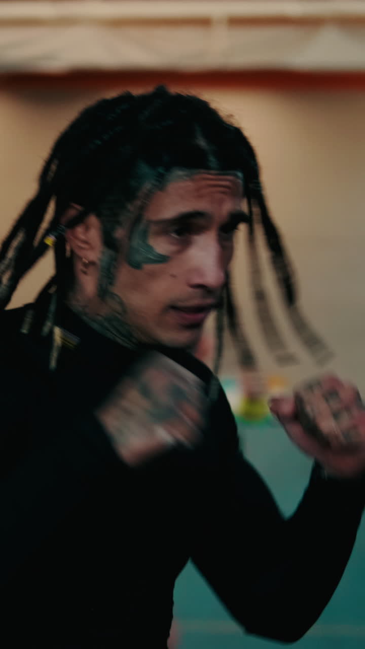 Primo piano di un uomo con dreadlocks e tatuaggi che si allena a fare boxe in palestra
