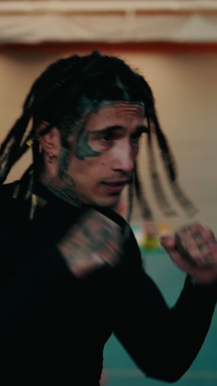 Primo piano di un uomo con dreadlocks e tatuaggi che si allena a fare boxe in palestra