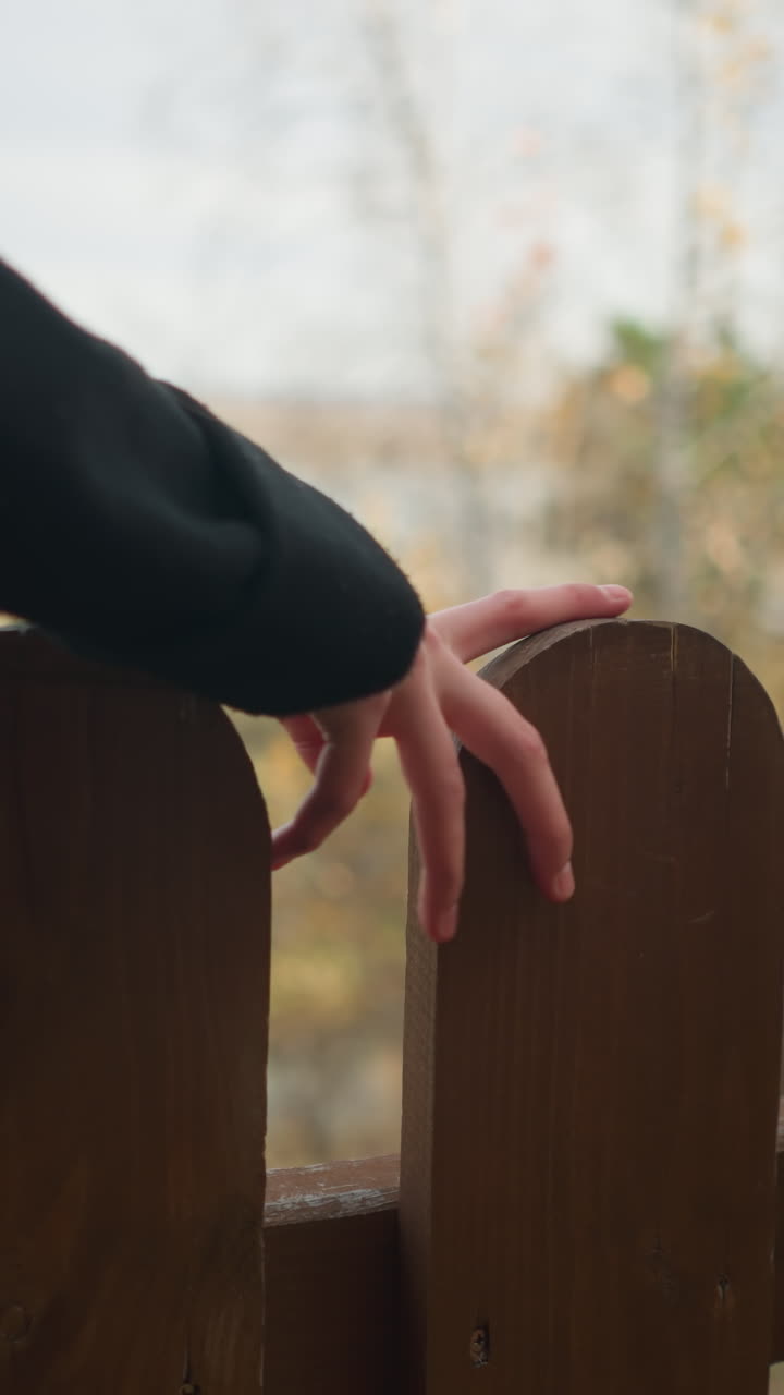 나무 울타리에 있는 여자의 손의 부드러운 만지는 은 나무와 가을의 배경에 있는 강으로, 자연과의 평온과 연결을 불러일으킨다.