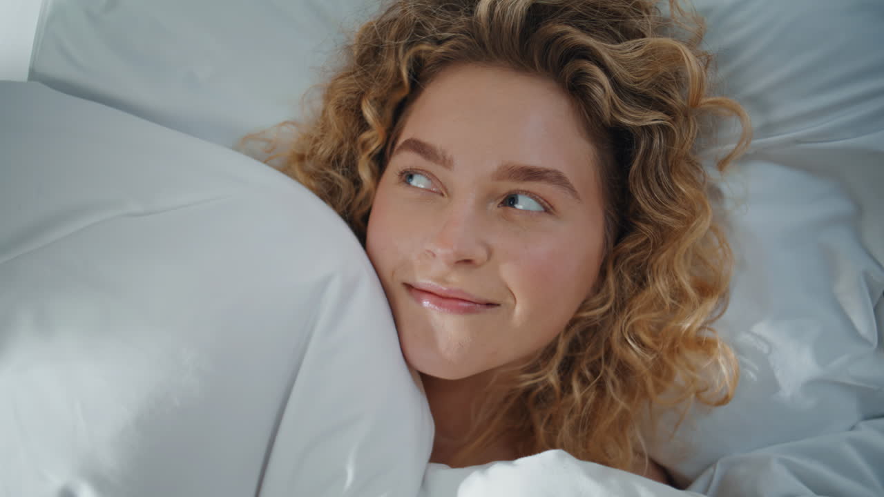 Gros plan sur une femme blonde heureuse se reposant sur un oreiller, cachée sous une couverture. Femme souriante rêvant.
