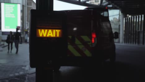 close up shot of a pedestrian crossing machine illuminated wait sign with a red london bus passing by