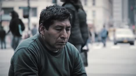 a man sits in deep contemplation on a bustling city street while people rush by, highlighting the contrast between stillness and movement in urban life.