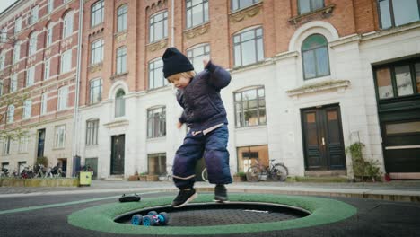 4-year-old-plays-with-an-RC-car,-jumping-on-a-trampoline-in-a-lively-Scandinavian-city-environment