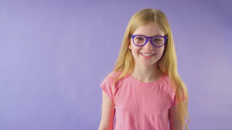 studio shot of smiling girl with long hair wearing blue glasses against purple background