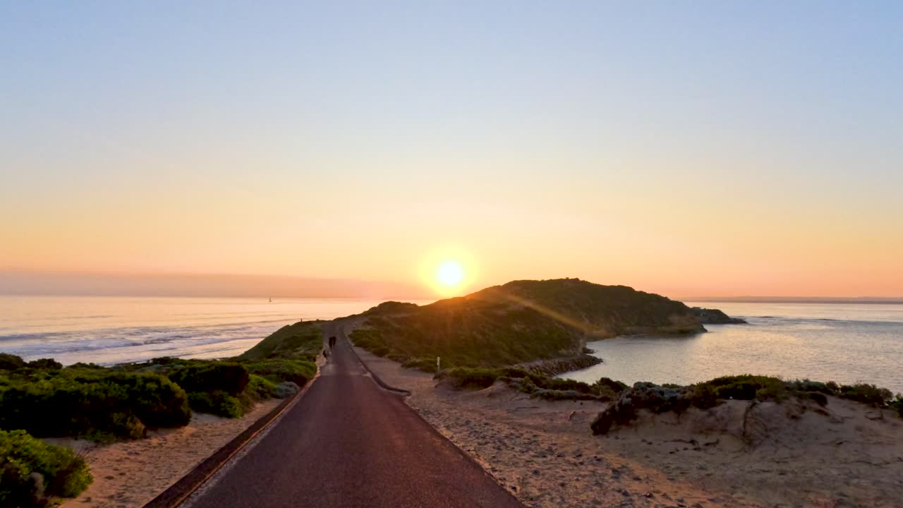 A serene sunset over a coastal road with lush greenery and ocean views, captured in warm, natural lighting