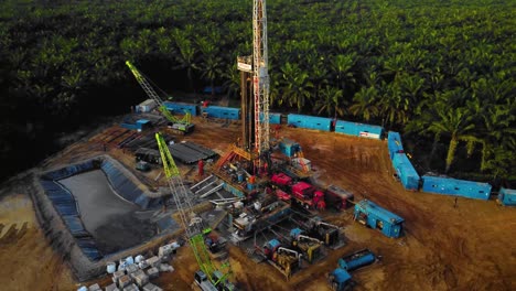 Cinematic-4K-Drone-Footage-of-Onshore-Drilling-Rig-equipment-structure-for-oil-exploration-and-exploitation-in-the-middle-of-jungle-surrounded-by-palm-oil-trees-during-sunset-and-high-oil-price