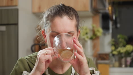 house wife drinks coffee from transparent glass cup with eyes closed, then drops cup gently while gazing at camera with calm satisfied expression in cozy kitchen