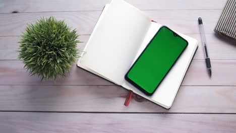 top view of smart phone with green screen and notepad on table