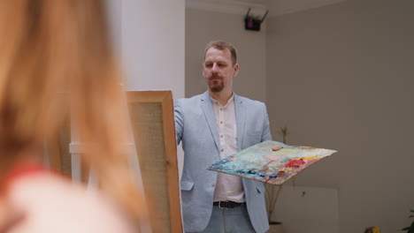 artist looks at model drawing portrait in studio. bearded art master holds color slab and woman adjusts hair in residence. creating beauty in designer studio