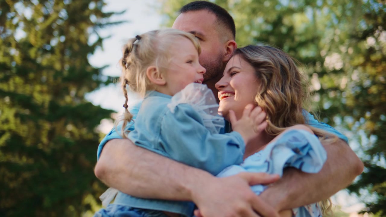 Abbraccio spontaneo di famiglia al parco. Genitori e figlio felici si godono un pomeriggio di sole. Connessione emotiva mostrata attraverso tocchi delicati. Ideale per biglietti d'auguri, campagne pubblicitarie o storie sui social media.