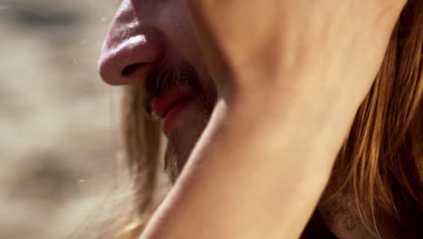 the woman lightly runs her fingers across the man's face as they sit together on the beach in the netherlands - close up