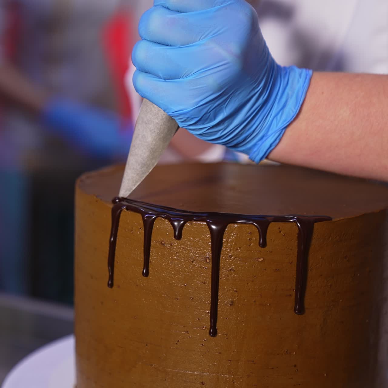 Decorazione di una torta con cioccolato. Primo piano. Le mani di un pasticcere, protette da guanti, spremono glassa di cioccolato fuso liquido sul bordo della torta