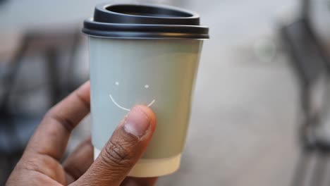 mano sosteniendo una taza de café de papel con un diseño de cara sonriente