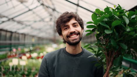 hombre sonriente sosteniendo una olla con árbol decorativo en un centro de jardín