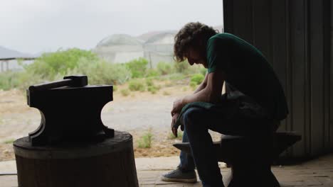 tired caucasian male blacksmith taking rest in workshop