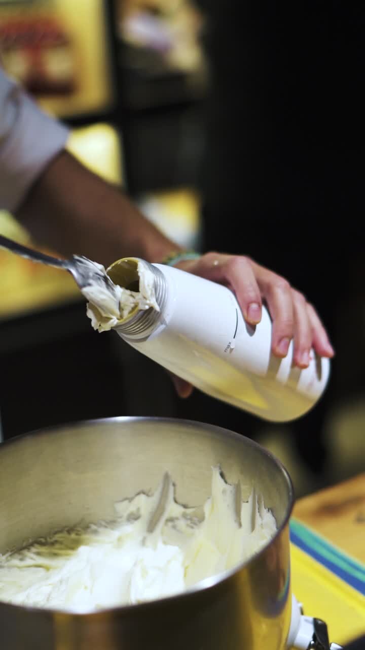 Un barista riempie un contenitore per panna montata con un cucchiaio da un grande contenitore di crema Chantilly