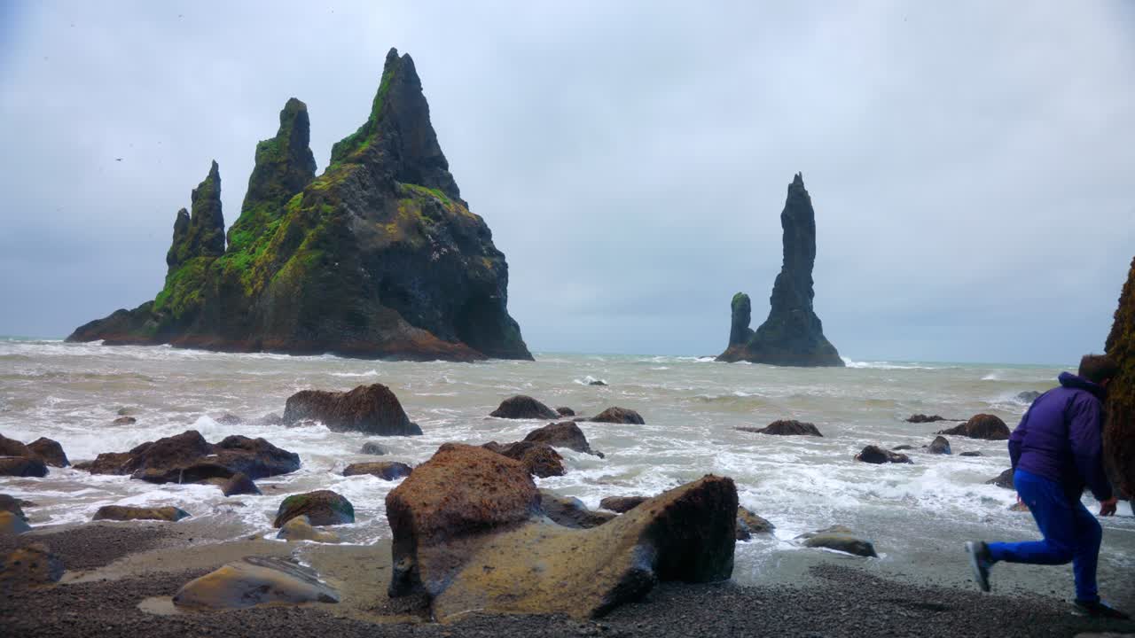 hombre saltando desde la gran roca marina en la playa de reynisfjara visitando el reynisdrangar en islandia