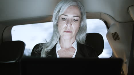 serious businesswoman working on laptop in car