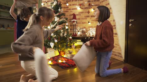 Fröhliche-Mutter-Bei-Kissenschlacht-Mit-Glücklichen-Kleinen-Töchtern-In-Einem-Mit-Weihnachtsbaum-Geschmückten-Zimmer