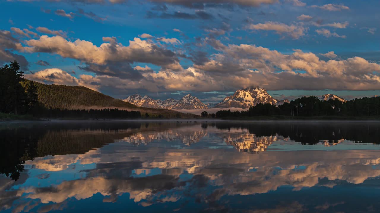 amplia vista del hermoso amanecer rosa y dorado en el lago espejo reflectante con montañas cubiertas de nieve y nubes gruesas que fluyen en el parque nacional grand teton, wyoming, estados unidos