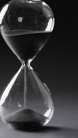vertical video of hourglass with sand pouring, copy space on black background