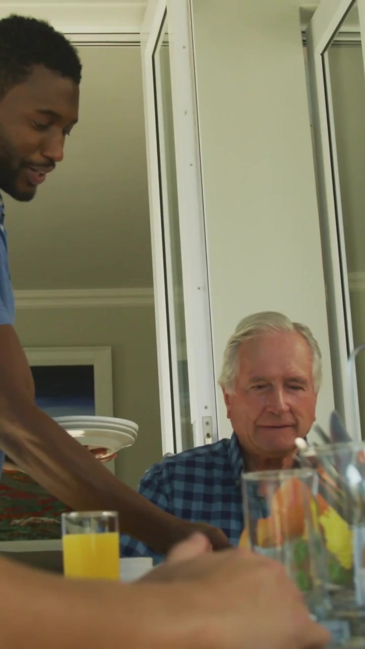 Vertical video: Standing man placing plates meal while senior watching tech charts overlaying table