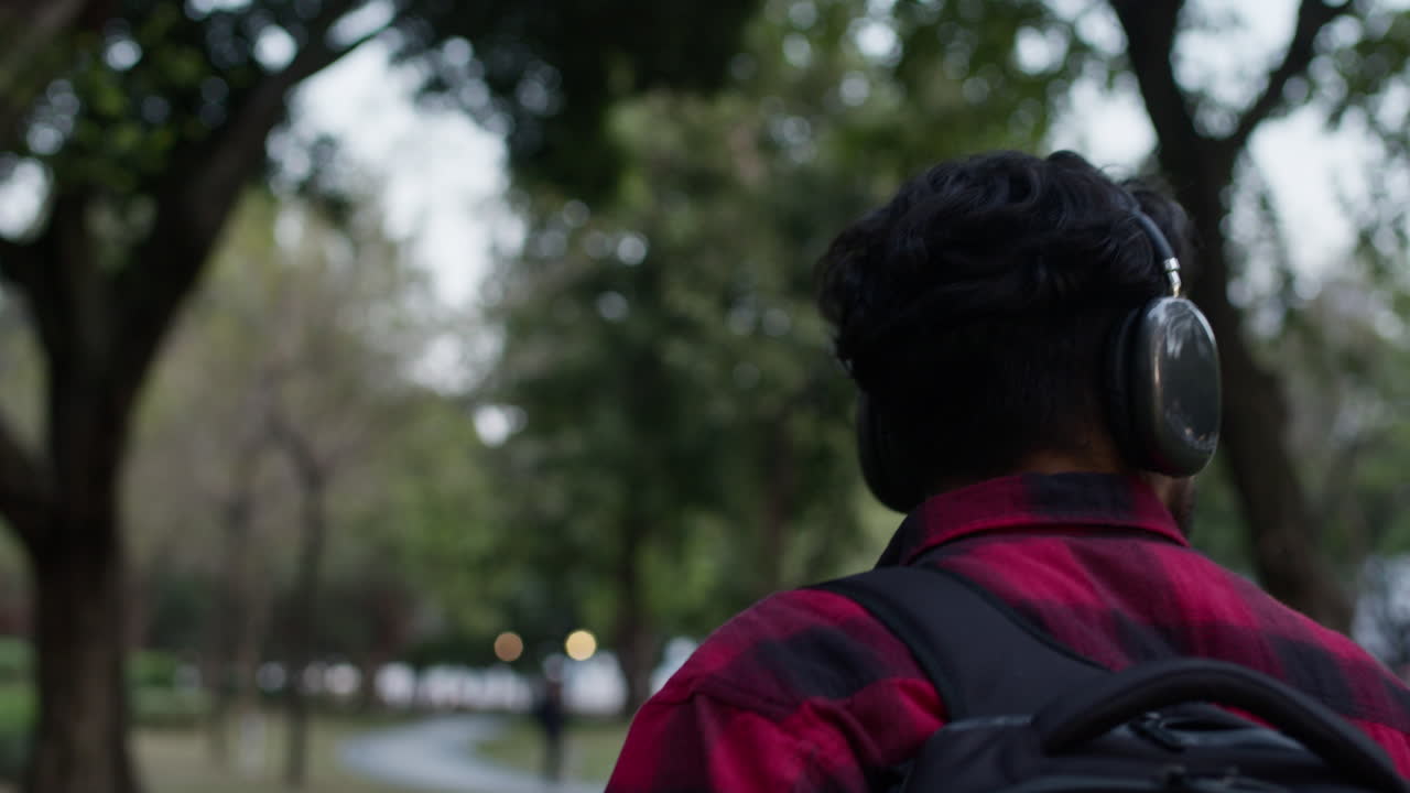 Man Walking in Park with Headphones and Backpack