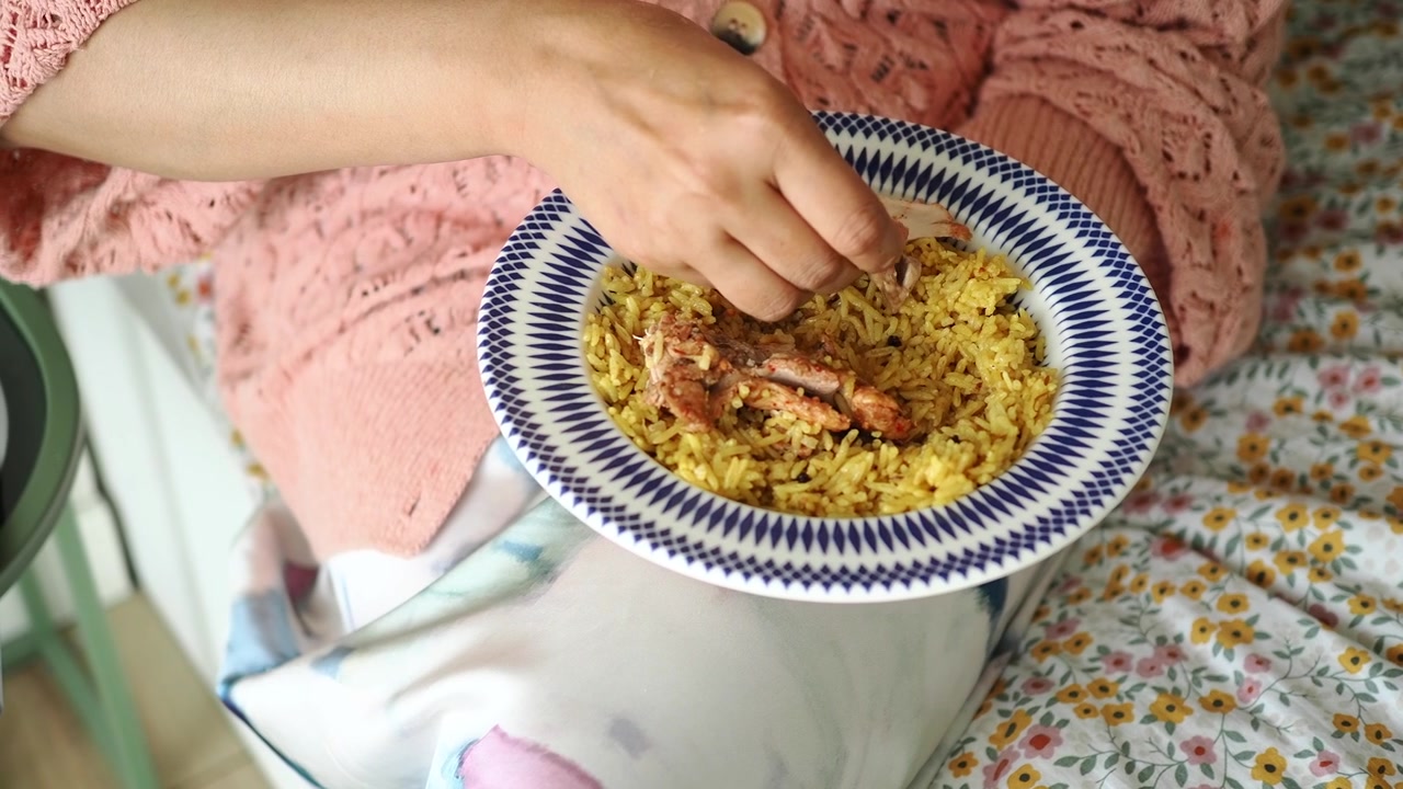 Persona che mangia pollo e riso da una ciotola.