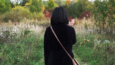 following shot of girl walking through park with autumn colors while swatting away flies