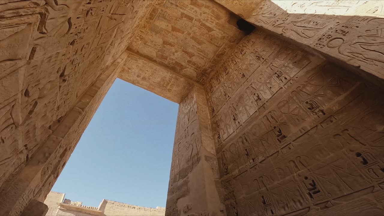 Cinematic upward shot from inside an ancient Egyptian temple, showcasing detailed hieroglyphics and wall carvings on towering stone structures.