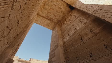 cinematic upward shot from inside an ancient egyptian temple, showcasing detailed hieroglyphics and wall carvings on towering stone structures.